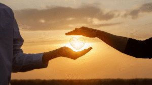Two hands holding a heart-shaped wire object in front of a sunset background.